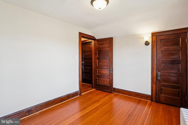 unfurnished bedroom with baseboards, lofted ceiling, and light wood finished floors