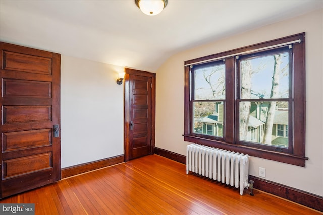 unfurnished room with radiator, lofted ceiling, baseboards, and wood-type flooring