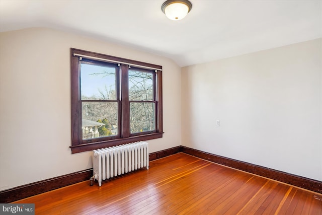 empty room with lofted ceiling, radiator heating unit, baseboards, and wood-type flooring