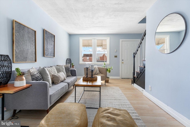 living room featuring stairs, baseboards, light wood-type flooring, and a textured ceiling