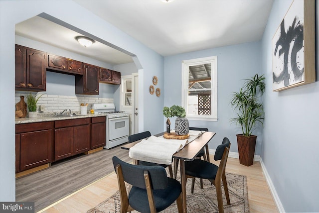 dining space with baseboards, arched walkways, and light wood-type flooring