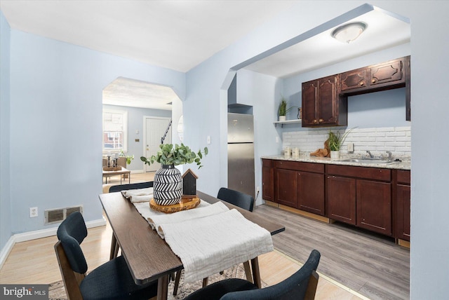 dining area featuring arched walkways, visible vents, light wood-style flooring, and baseboards