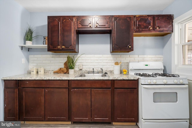 kitchen with light stone countertops, open shelves, a sink, decorative backsplash, and white gas range oven