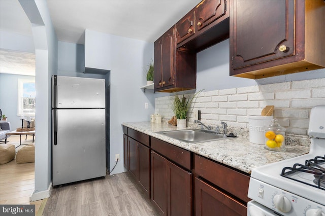 kitchen featuring white gas stove, freestanding refrigerator, a sink, light wood-style floors, and backsplash