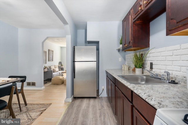 kitchen featuring visible vents, a sink, freestanding refrigerator, arched walkways, and light wood finished floors