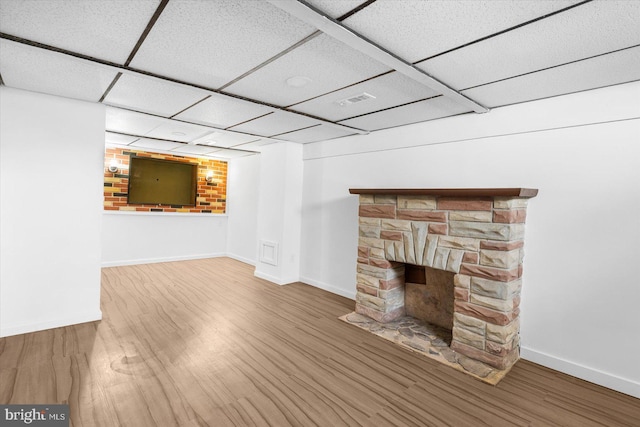 unfurnished living room featuring a drop ceiling, baseboards, a stone fireplace, and wood finished floors