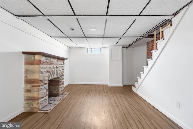 unfurnished living room with baseboards, a fireplace, a drop ceiling, stairs, and light wood-style floors