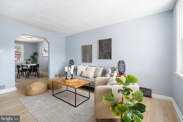 living room with wood finished floors, visible vents, baseboards, arched walkways, and a textured ceiling