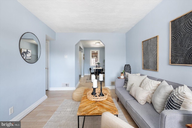 living room featuring baseboards, arched walkways, a textured ceiling, and light wood finished floors