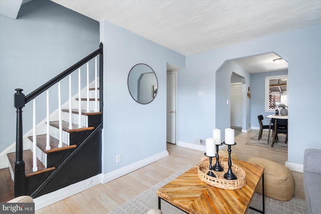 living area featuring baseboards, arched walkways, a textured ceiling, and wood finished floors