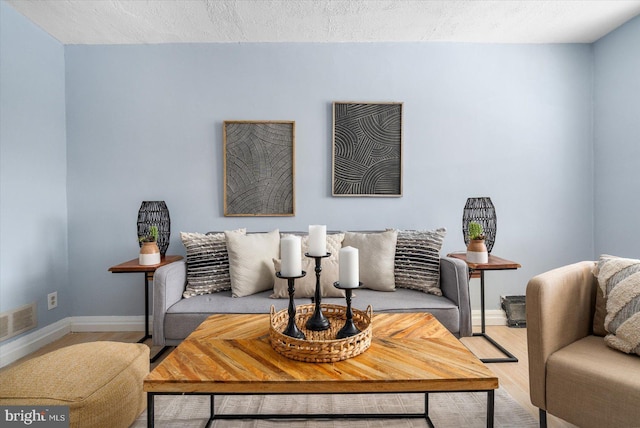 living room featuring visible vents, a textured ceiling, baseboards, and wood finished floors