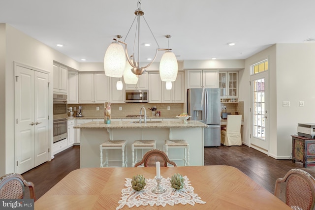 kitchen featuring dark wood-type flooring, a center island with sink, a sink, tasteful backsplash, and appliances with stainless steel finishes