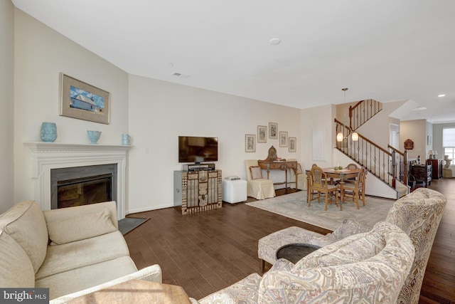 living room featuring a glass covered fireplace, stairway, wood finished floors, and visible vents