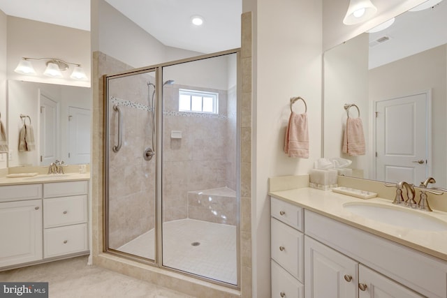 bathroom featuring visible vents, a stall shower, two vanities, and a sink