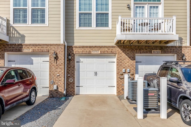 exterior space with a garage, brick siding, a balcony, and driveway