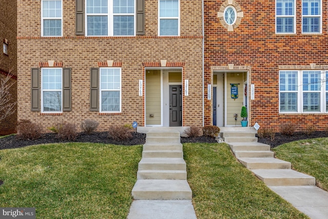 view of exterior entry featuring brick siding and a lawn