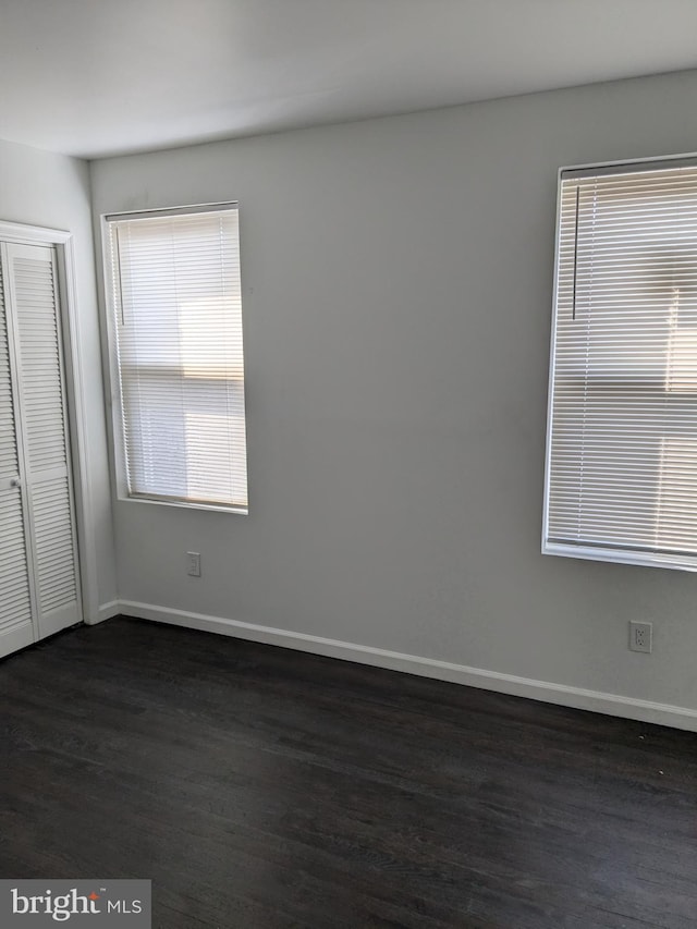 unfurnished bedroom with a closet, baseboards, and dark wood-style flooring