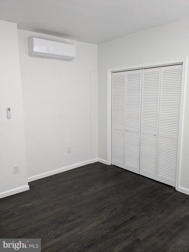 unfurnished bedroom featuring an AC wall unit, baseboards, dark wood-type flooring, and a closet