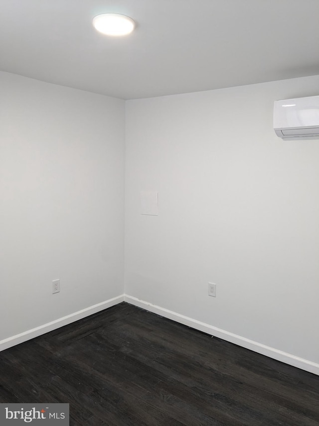 empty room featuring baseboards, an AC wall unit, and dark wood finished floors