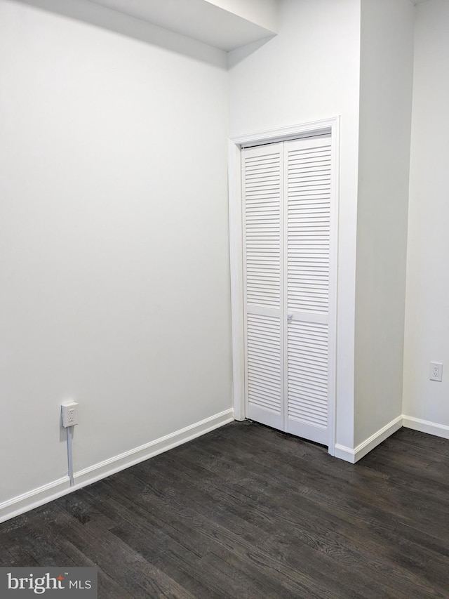 unfurnished bedroom featuring a closet, baseboards, and dark wood-style floors