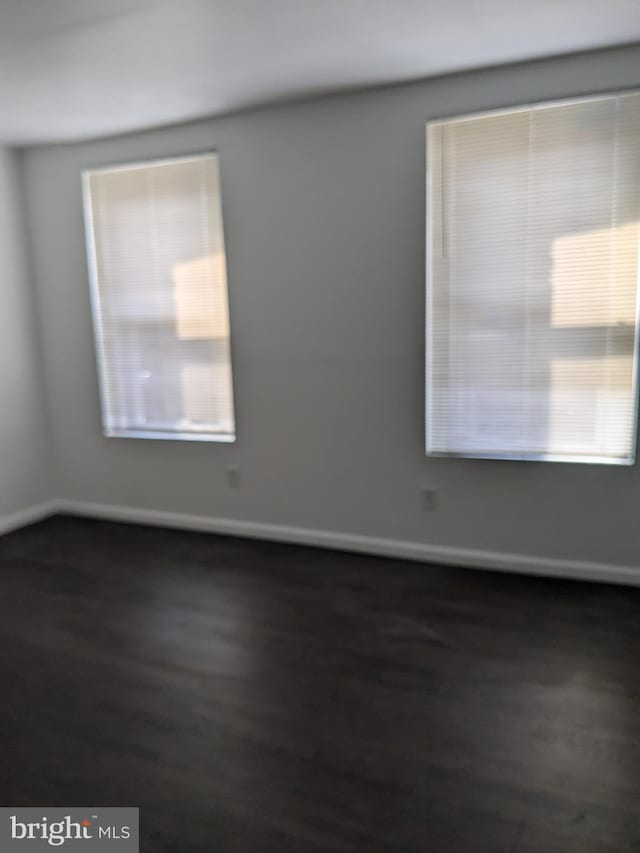 unfurnished room featuring baseboards, plenty of natural light, and dark wood-type flooring