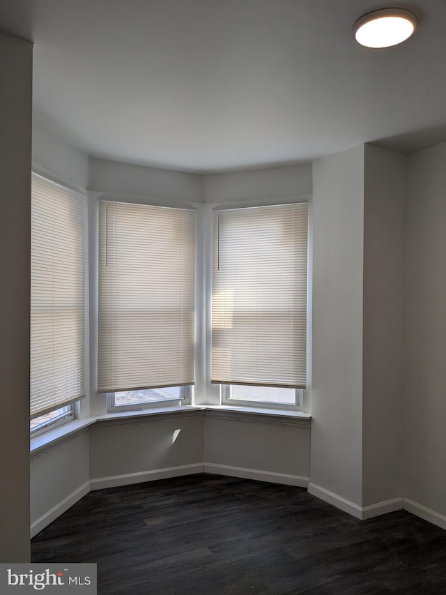 unfurnished room with baseboards, plenty of natural light, and dark wood-type flooring