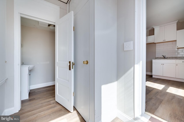 bathroom featuring decorative backsplash, a sink, baseboards, and wood finished floors