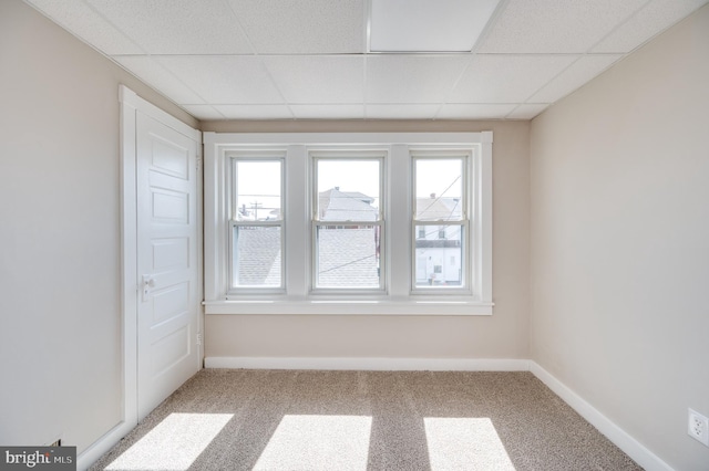 empty room featuring carpet flooring, plenty of natural light, a paneled ceiling, and baseboards