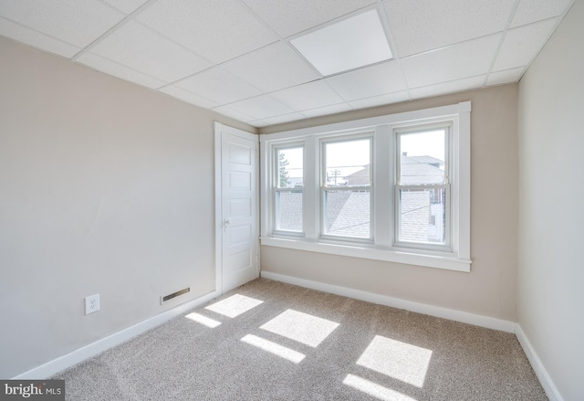 carpeted spare room featuring baseboards and a drop ceiling