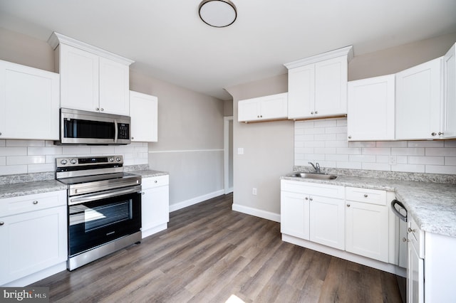 kitchen featuring tasteful backsplash, appliances with stainless steel finishes, wood finished floors, white cabinetry, and a sink