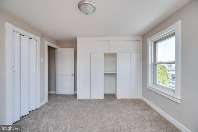 unfurnished bedroom with light carpet, two closets, and baseboards