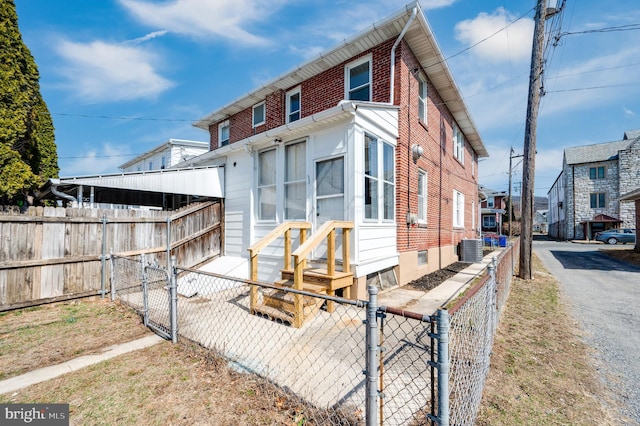 exterior space with a gate, entry steps, a fenced front yard, brick siding, and central AC unit