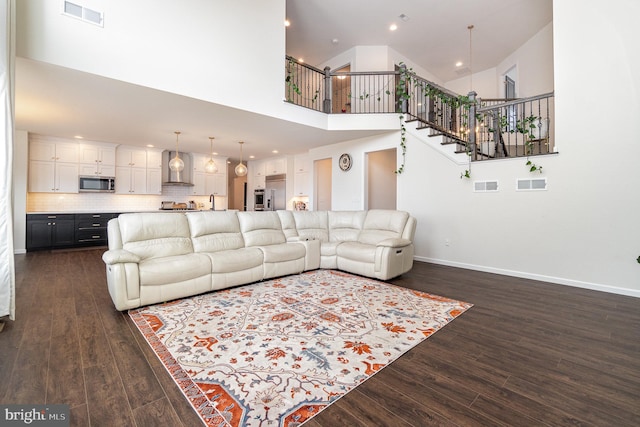 living area with dark wood-style floors, visible vents, stairway, and a high ceiling