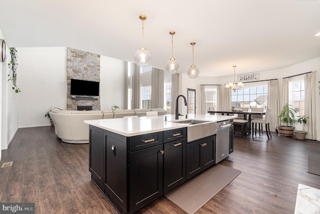 kitchen with dark cabinetry, dark wood-style floors, light countertops, stainless steel dishwasher, and a notable chandelier