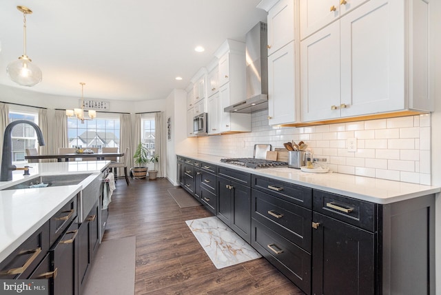 kitchen with stainless steel appliances, wall chimney exhaust hood, light countertops, and white cabinetry