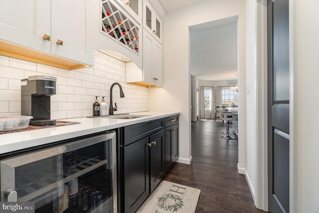 kitchen featuring dark wood-style floors, beverage cooler, a sink, light countertops, and tasteful backsplash