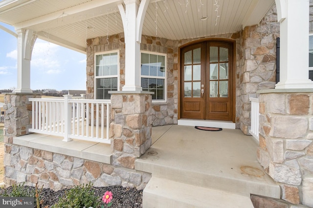 property entrance featuring french doors, stone siding, and covered porch