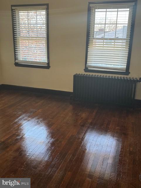 empty room with radiator, dark wood-style floors, and baseboards