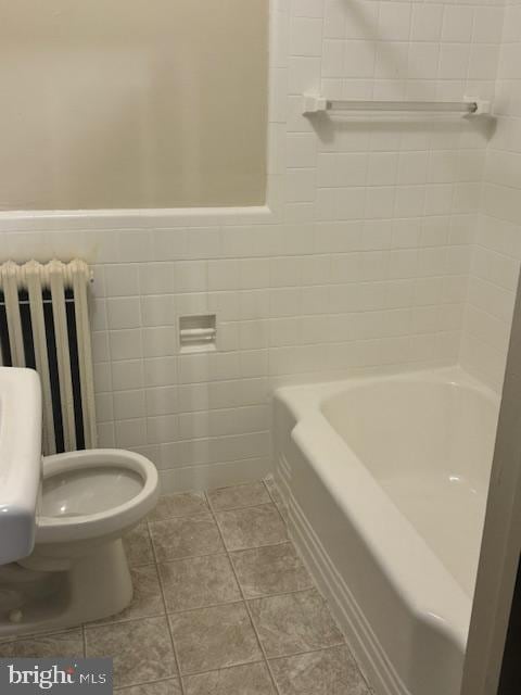 bathroom with a bath, radiator heating unit, tile patterned flooring, tile walls, and toilet