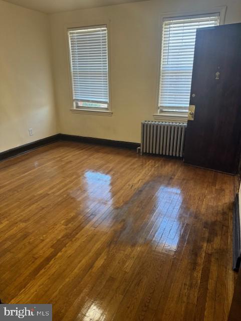 unfurnished room featuring hardwood / wood-style flooring, radiator heating unit, and baseboards