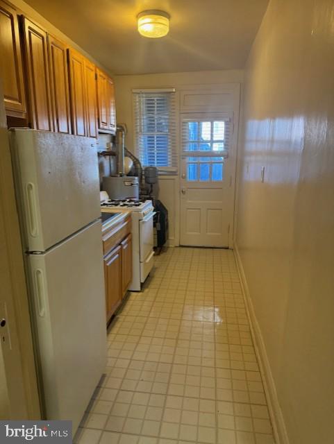 kitchen with brown cabinetry, white appliances, and baseboards