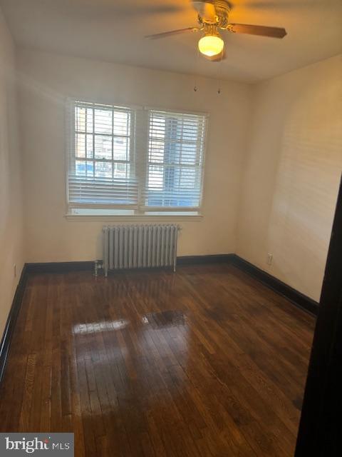 spare room with baseboards, wood-type flooring, radiator, and ceiling fan