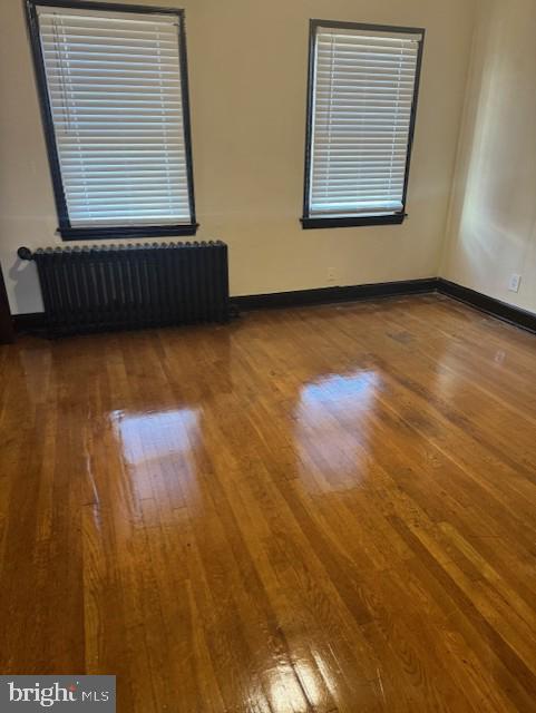 spare room featuring baseboards, wood finished floors, and radiator heating unit