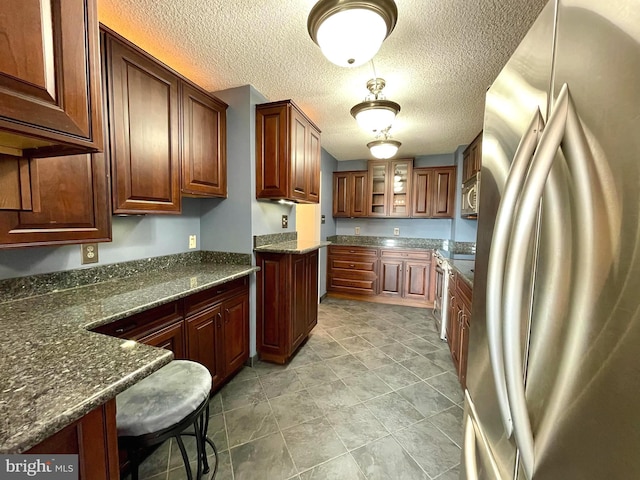 kitchen with dark stone countertops, a textured ceiling, stainless steel appliances, and glass insert cabinets