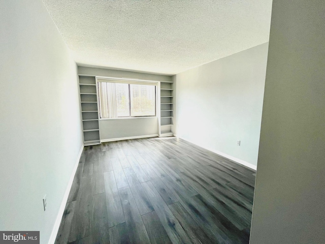 spare room with a textured ceiling, dark wood-type flooring, and baseboards