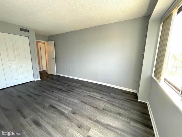 unfurnished bedroom featuring dark wood-type flooring, visible vents, baseboards, and a closet