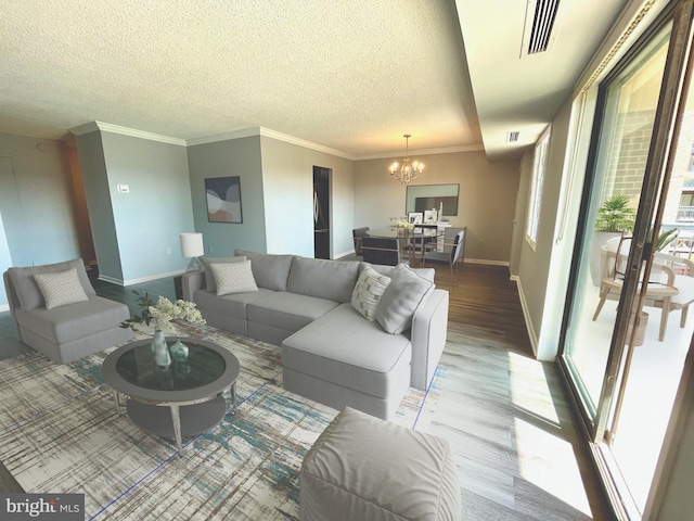 living area featuring visible vents, a notable chandelier, a textured ceiling, wood finished floors, and baseboards