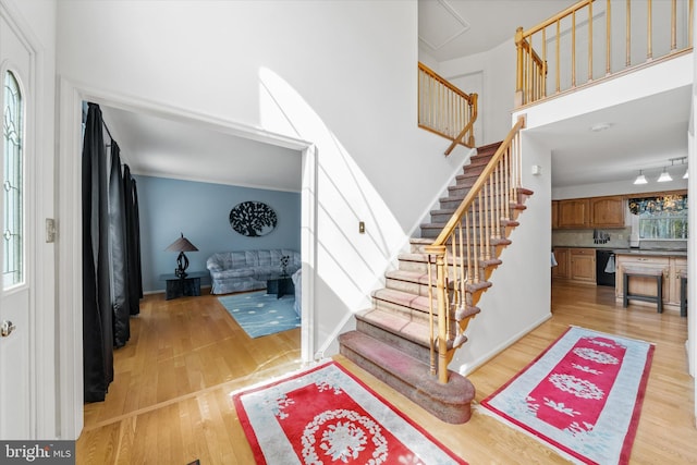 foyer entrance with stairway, baseboards, a high ceiling, and light wood-style floors