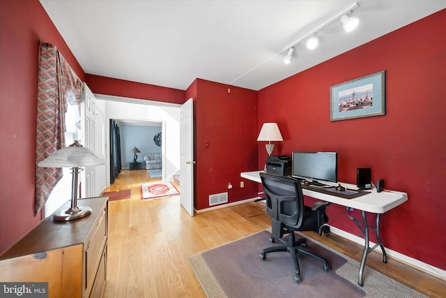 home office with visible vents, light wood-style flooring, rail lighting, and baseboards