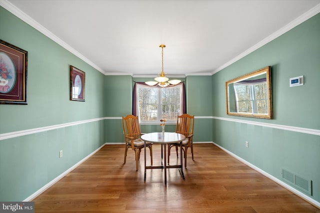 dining space with crown molding, wood finished floors, visible vents, and baseboards